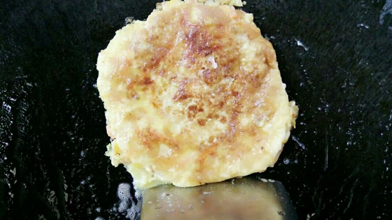 宝宝辅食:田园鸡蛋饼,因为油倒多了所以煎熟的田园鸡蛋饼用锅勺顶在锅上角掉油