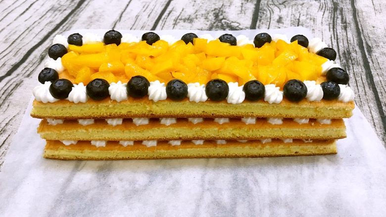 水果蛋糕,铺上最后一层蛋糕片，奶油和蓝莓间隔开，中间铺上黄桃粒