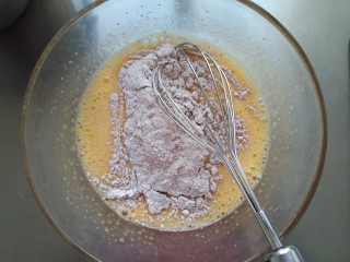 巧克力千层毛巾卷,将一半过筛好的面粉倒入鸡蛋液中，搅匀。