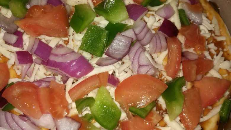 牛肉蔬菜披萨,铺上西红柿，青椒和洋葱丁，撒适量披萨草