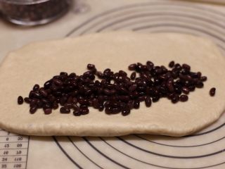 蜜豆爱心吐司,松弛好的面团用擀面杖擀成长方形，上铺蜜红豆卷起入模具。