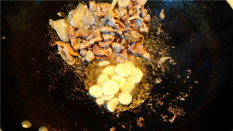 香菇大蒜炒肉,肉片变色，就将肉片推到锅边，将蒜片放入锅里的底油里爆香。
