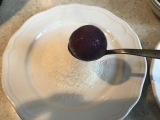 紫薯糖心糯米滋,把椰蓉倒进盘子里，用勺子轻轻的捞起一个丸子放到椰蓉里