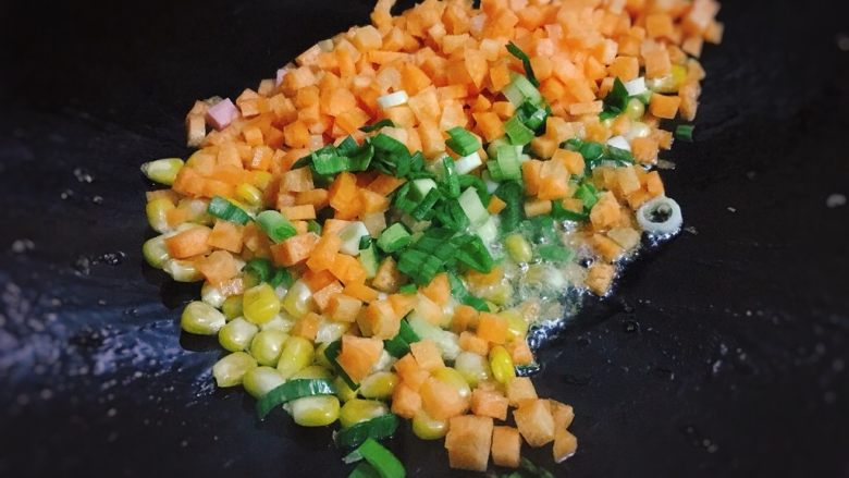 五彩玉米火腿炒饭,炒至玉米粒微微膨胀，倒入胡萝卜丁和蒜末，一起翻炒20秒。