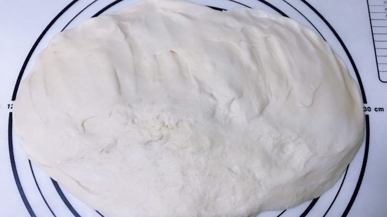爆浆肉松面包,案板上撒少许干粉，手沾少许干粉，取出发酵好的面团轻拍排气
