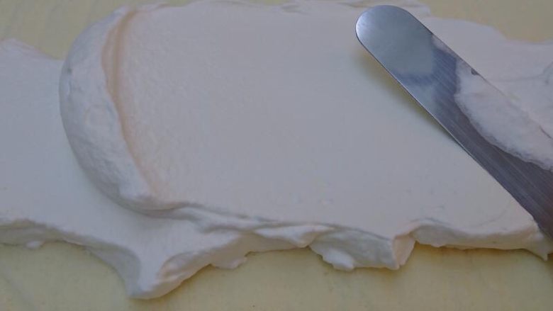 樱花蛋糕卷,蛋糕體放涼後，上面鋪一張新的烘培紙將蛋糕翻面，使上色那面朝下無上色那面朝上。倒入打發的鮮奶油霜，均勻抹平表面，尾端處預留1cm，避免捲蛋糕時溢出奶油霜。