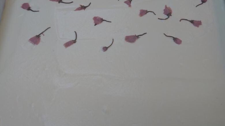 樱花蛋糕卷,在麵糊表面點綴幾朵櫻花(可省略)。桌上墊塊布將烤盤由上而下輕震2下，使大氣泡震出。