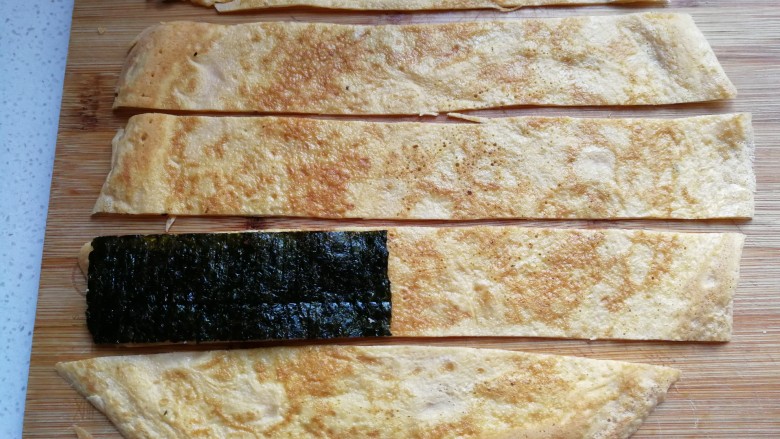 年夜菜~锦绣苔味香肠卷,摊好的鸡蛋饼取出光面朝下，用刀分切成与海苔同宽的条状