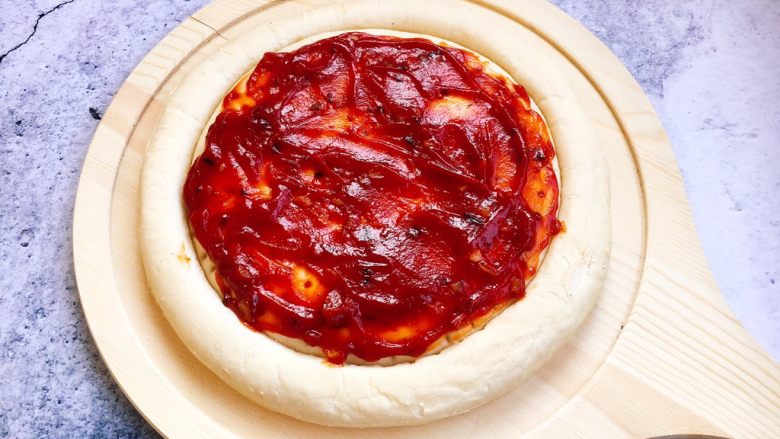 做年货 春节聚会宝贝们爱吃的 鲜虾黑胡椒牛肉粒培根披萨,将3勺秘制番茄酱均匀的涂在披萨饼上。