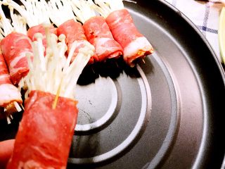 经光波烘焙的金针菇培根卷,再用牙签别上肉卷，摆放于光波炉的烤盘内。
