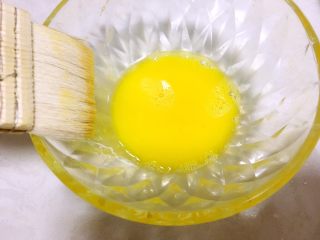 五仁月饼,打一颗蛋黄在干净的碗内，尽量带一些蛋白进来，这样搅拌好的蛋黄液不会太干，用羊毛刷沾点蛋黄液，之后在碗壁挂掉多余的蛋黄液