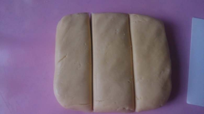 彩虹爱心饼干,把面团从盆中取出，放到垫板上，用手揉捏成团，然后分成三份。