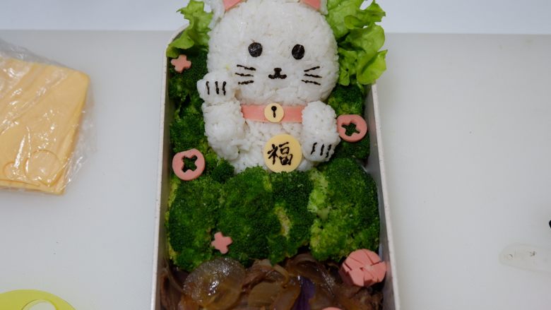 卡通招财猫牛肉饭便当盒,再取适量火腿片压出小花装饰即可。