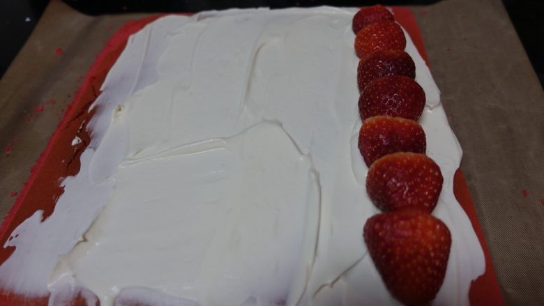 红丝绒波点蛋糕卷,待蛋糕完全冷却，涂抹一层奶油。草莓排排坐如图排好位置。借助油布从有草莓的一边卷起来，放入冰箱冷冻5-10分钟。