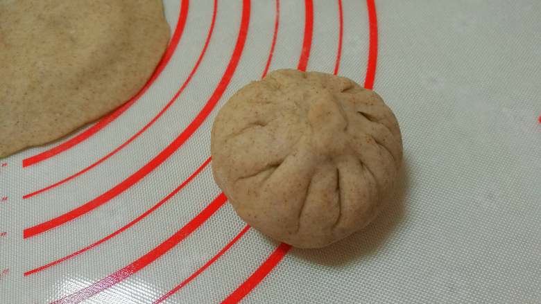 黑麦南瓜豆沙包,用手捏成包子状，捏紧收口揉圆，收口朝下放在揉面垫上。