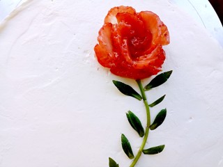 情人节玫瑰花蛋糕,取一个草莓，切成片，然后做成玫瑰花的形状，摆在合适的位置上，用草莓蒂连接成花茎，用草莓蒂周边的小叶摆成花叶的样子。