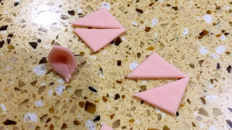 卡通馒头,把压完猪鼻子剩的粉色面皮 切成一个四方型、再等分成四个小方块、一个小方块再切成两个三角形用来做猪耳朵
三角朝里对折 可以粘一点点牛奶帮助粘合