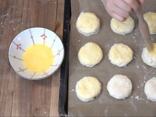 3分钟淡奶油司康,烤盘上铺一张烘焙纸，把一个鸡蛋打散，涂抹在司康饼的表面和四周。