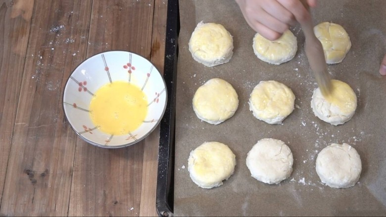 3分钟淡奶油司康,烤盘上铺一张烘焙纸，把一个鸡蛋打散，涂抹在司康饼的表面和四周。