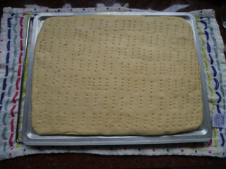 香葱肉松面包卷,将面团擀开成烤盘合适的大小。28*28的烤盘适合此配方。用叉子在放入烤盘的面上细密的扎上小孔。