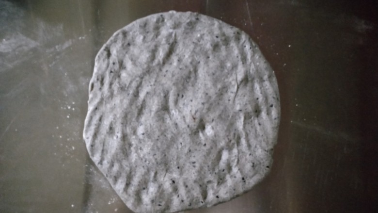 黑芝麻软欧包,发酵好的面团取出来放在揉面垫上，轻拍面团帮助它排气。
