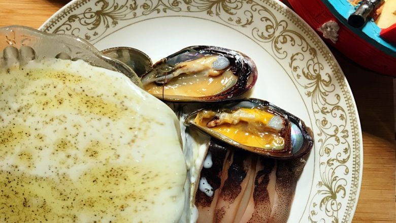 光波烘焙的芝士白汁焗海鲜饭,将调料奶液倒入盛有海鲜的盘子内。