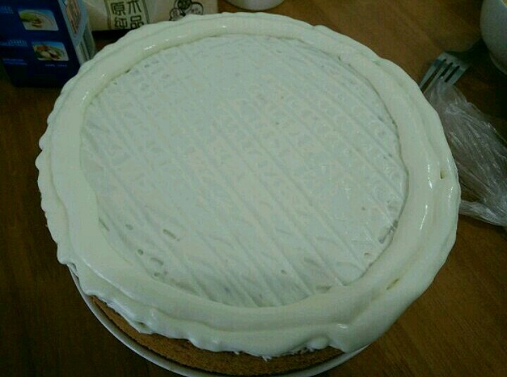 酸奶淋面蛋糕,取一半的奶油倒在蛋糕上，用刮板刮出纹路。剩下的一半装到裱花袋，剪个口，在蛋糕周围挤一圈奶油。