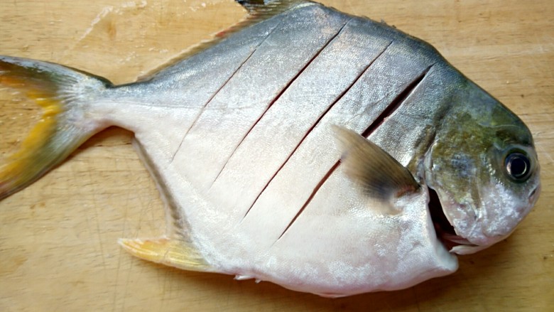 秘制红烧鲳鱼,鱼放在菜板上斜切几刀