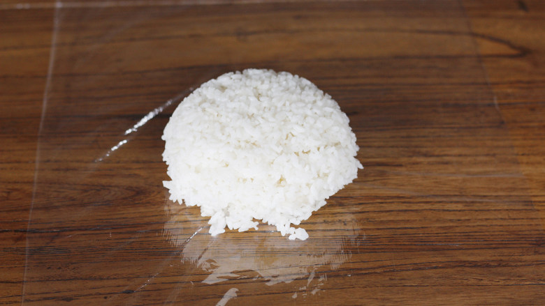 仙貝！仙貝！（剩米饭版）,首先在操作台上铺上一张保鲜膜，保鲜膜的长度尽量长一点，因为在后续是要掀过来改善米饭的。
将米饭倒在准备好的保鲜膜上。