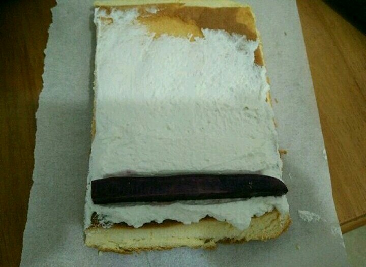 紫薯蛋糕卷,取适量淡奶油抹在蛋糕上，再放上紫薯条，然后卷起来，包好放冰箱冷藏定型一个小时。