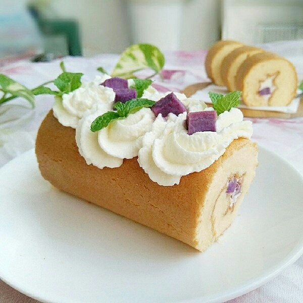 紫薯蛋糕卷,取出定型好的蛋糕卷，把奶油挤到上面。放几颗紫薯粒和薄荷叶。