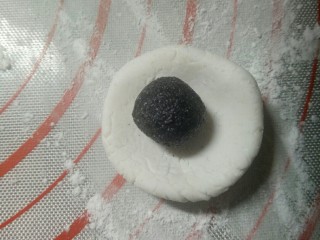 熊猫汤圆～幸福团团圆圆,硅胶垫上撒些糯米粉，取一个10克的白面团揉圆按扁，放入黑芝麻糖馅