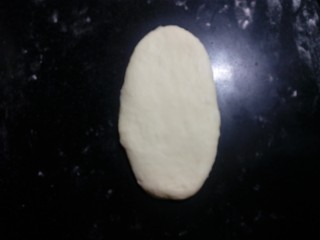 炼奶辫子面包,取一份面团，光面向上，擀成椭圆形。