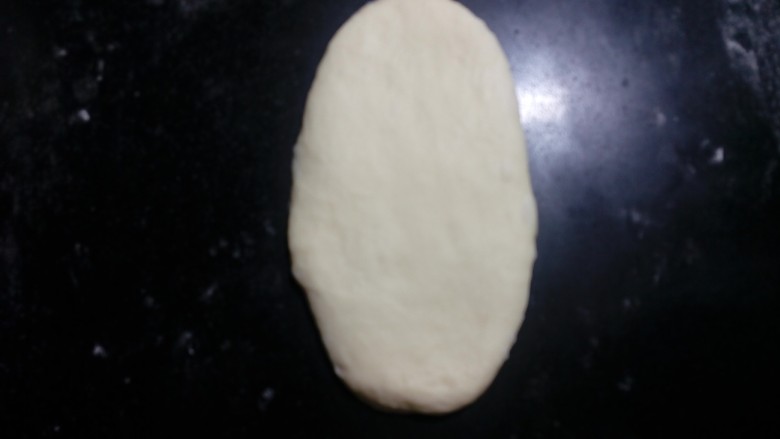 炼奶辫子面包,取一份面团，光面向上，擀成椭圆形。