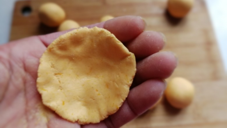 南瓜豆沙小汤圆,取一个糯米团先用手掌压扁，然后把四周用手捏薄，使其成四周薄中间厚的形状