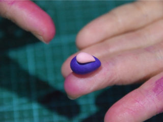 凹造型的独角兽玛琳糖,更小一点的粉色，做成水滴状，搭在紫色的翻糖膏上。
