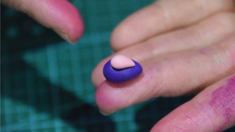 凹造型的独角兽玛琳糖,更小一点的粉色，做成水滴状，搭在紫色的翻糖膏上。