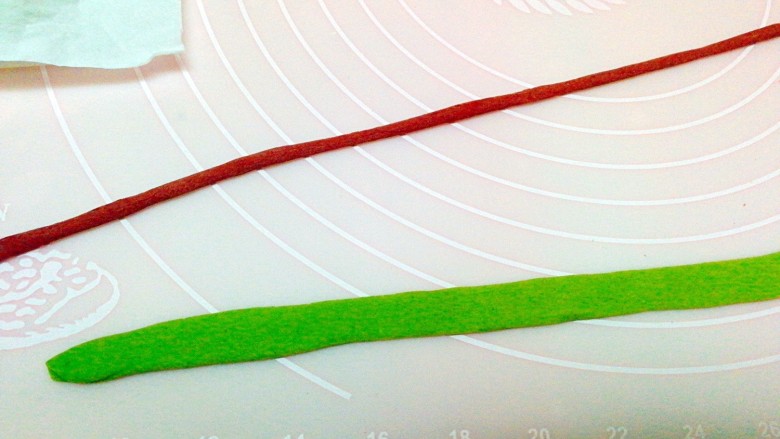 雪宝宝&雪花馒头,绿色面团擀薄，然后把深红曲面团搓成细条，放在蓝面片上，再用擀面杖擀平，切成长条，做围巾