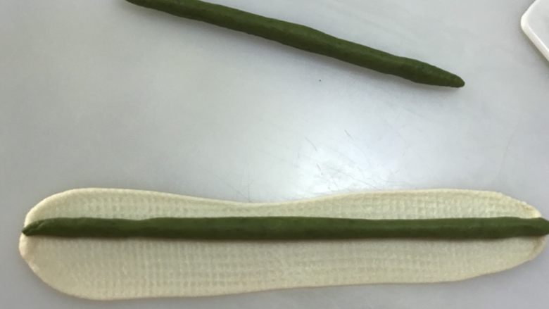 玫瑰花吐司,分别取3个12克的绿色面团搓长成棒状，再分别取3个12克的白色面团擀开擀长，把绿色面团包住，捏紧收口处。