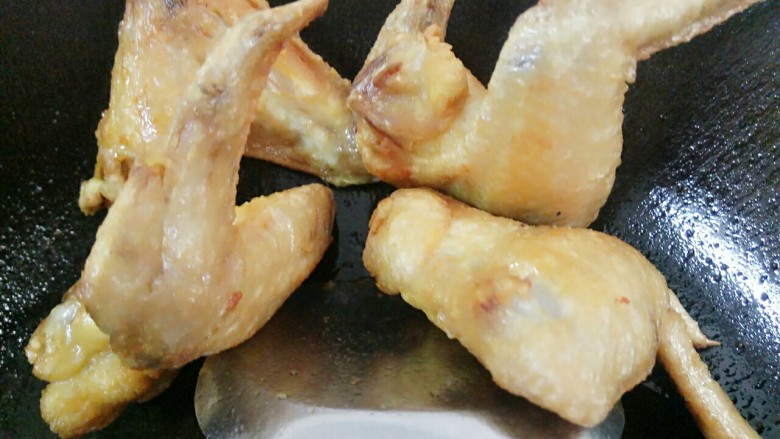 芝麻香沙茶酱鸡翅,煎熟的鸡翅用锅勺顶在锅边掉油
