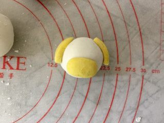 小萌狗黑芝麻汤圆,用小块黄色粉团，捏成椭圆形，如图分别沾水黏在白色汤圆上，做小狗的耳朵和嘴部。