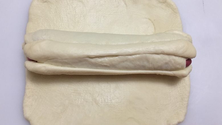 爱心💗吐司,剩下的白色面团擀压成约22厘米*10厘米的面皮，把14倒置于面皮上。拉起靠近自己这一侧的面皮与另一侧对齐。