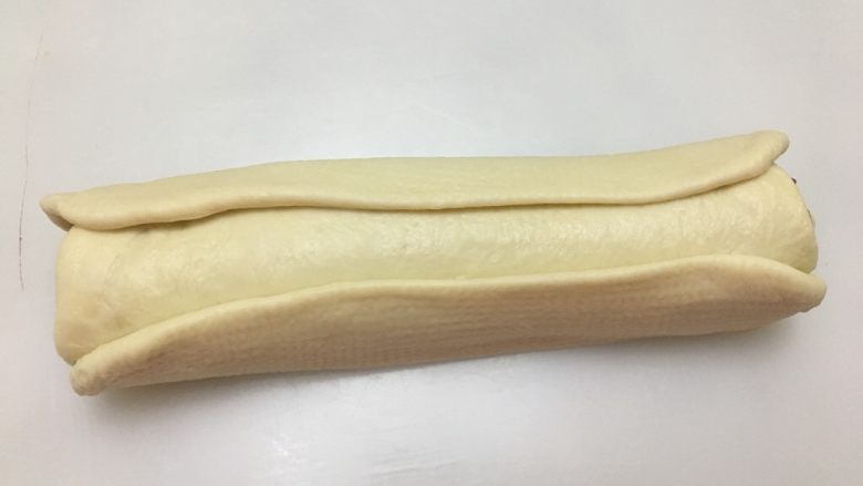 爱心💗吐司,把12翻面，取两个30克的白色面团，擀压成约22厘米*3厘米的面皮，放在左右两侧。