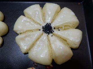 椰蓉花朵面包,发酵至1.5倍大即可。取出刷蛋液，中心处用黑芝麻装饰。