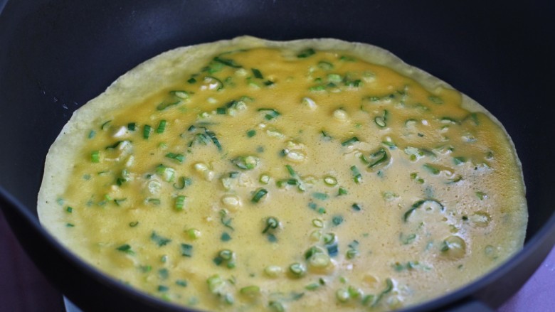 葱花鸡蛋饼,轻轻转动锅体，使鸡蛋面糊均匀的向锅的四周散开，摊成圆饼皮