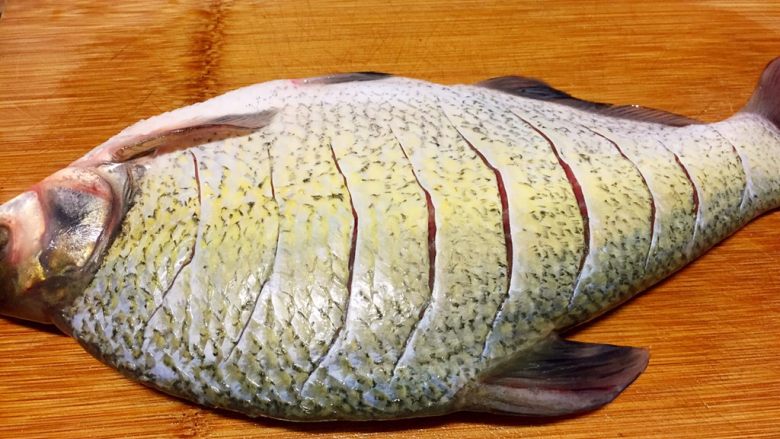 川味干烧臊子鱼,鱼洗净用刀在鱼身两面上划成如图的切口。