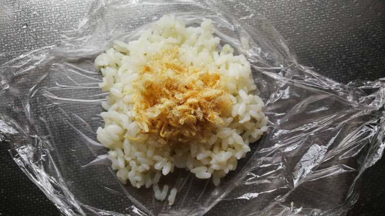 熊猫-鸡排便当,蒸熟米饭下面铺保鲜膜放入一勺米饭，中间可以加入肉松，也可以不放。团成圆球做熊猫的头。每个70g左右。
