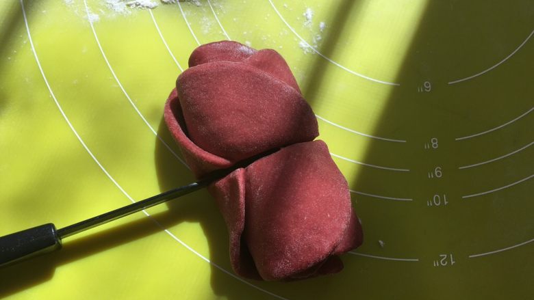 双色玫瑰花面包,卷好后，用刀沿着筷子压出的痕迹，从中间切开，玫瑰花就做好啦，底下撒点干粉，放一旁备用