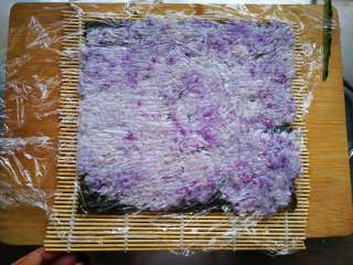 翻转花朵寿司,竹帘上面铺海苔，海苔上面铺一层紫色米饭，米饭上面铺层保鲜膜。
