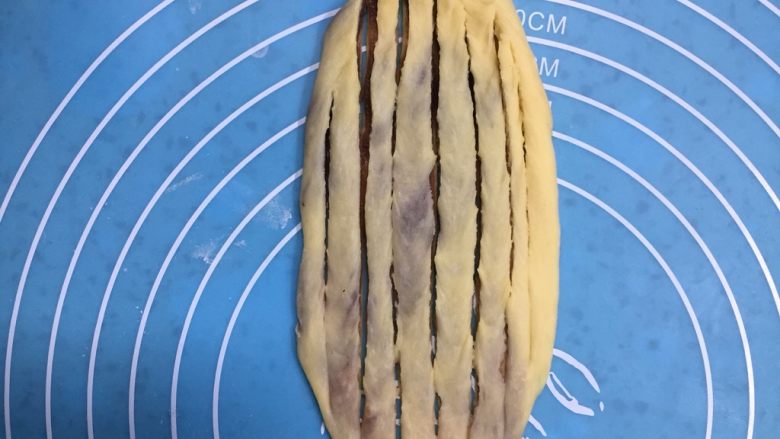 扭扭层层豆沙面包,用擀面杖轻轻的擀成薄薄的椭圆形，再用切刀划口，除两头不划断中间刀口划断